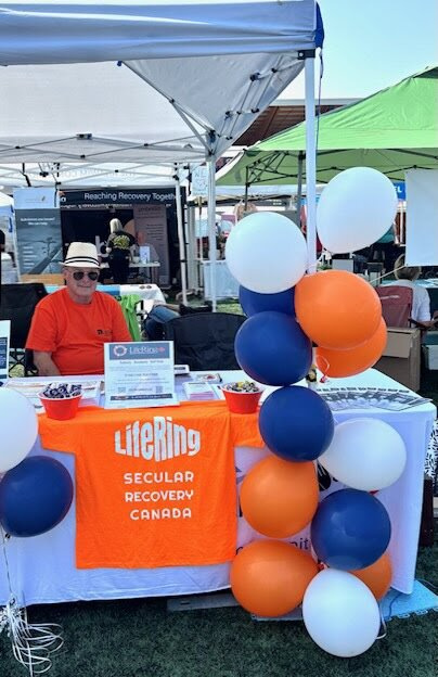 Dave seated at the LifeRing Canada table in his sunhat
